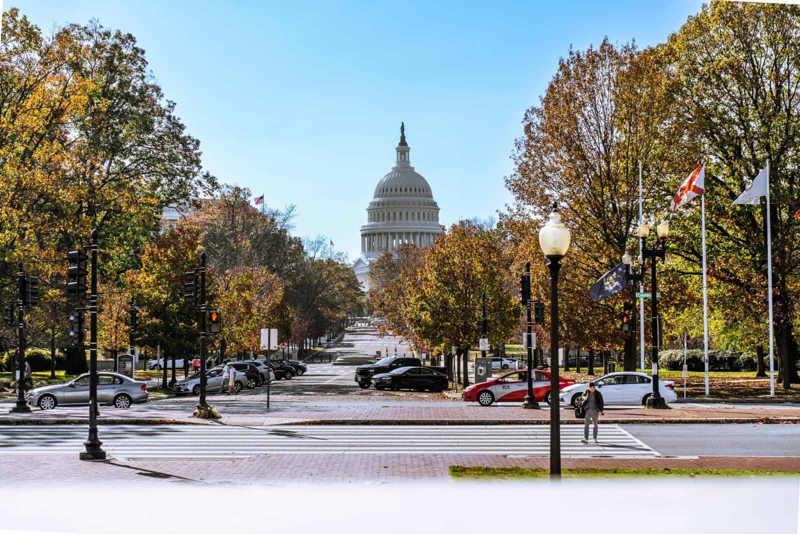 The U.S. Capitol in the distance, with autumn leaves on the trees and Washington, D.C. residents walking in the foreground.